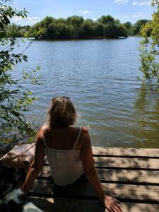 woman sitting quietly by the water reflecting during a gratitude practice