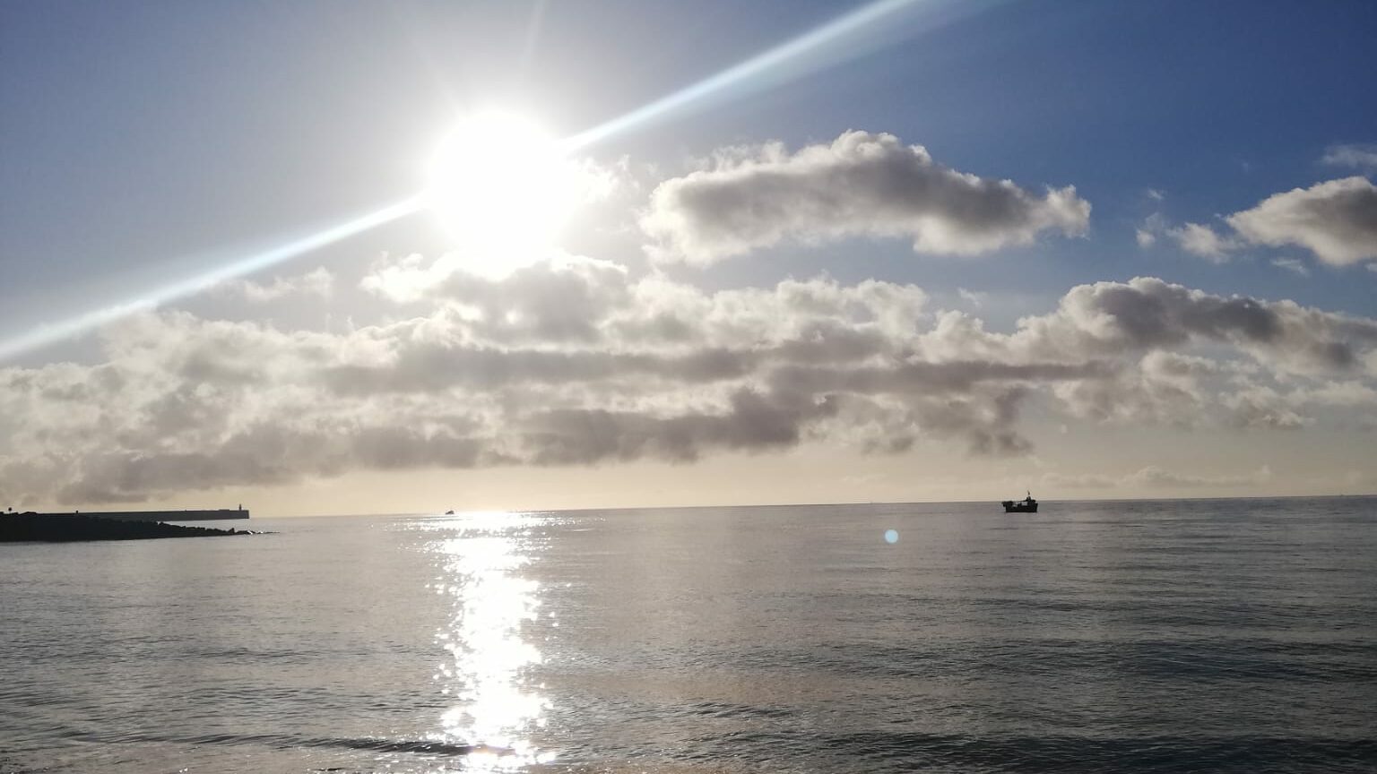 Sunshine reflecting across a calm sea with soft clouds in the sky, capturing a quiet moment of stillness and enoughness